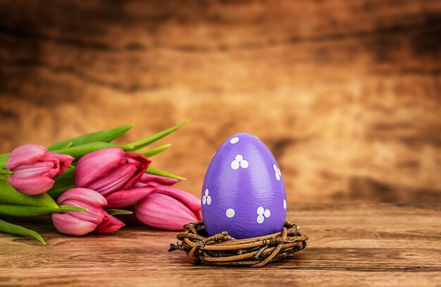 Un huevo de Pascua en un nido y tulipanes rosados en una mesa de madera con fondo desenfocado