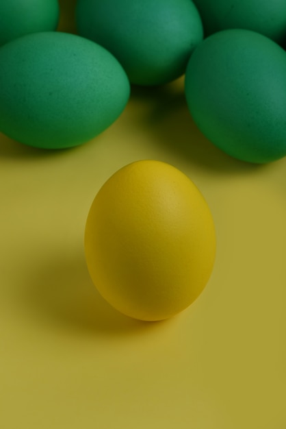 Un huevo de Pascua pintado amarillo se coloca frente a los huevos verdes sobre un fondo amarillo