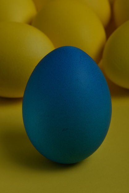 Un huevo de Pascua pintado azul se coloca delante de los huevos amarillos sobre un fondo amarillo