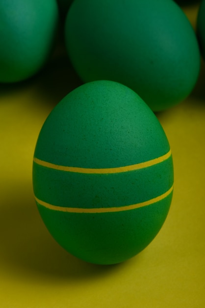 Un huevo de Pascua pintado de color verde con dos franjas amarillas se coloca frente a los huevos verdes sobre un fondo amarillo