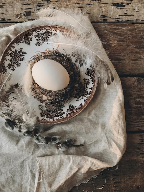 Foto huevo de pascua en plumas de nido plato vintage servilleta de lino ramas de sauce en mesa rústica