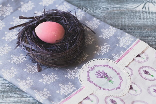 Huevo de Pascua rosa en un nido morado decorativo sobre el mantel hecho a mano