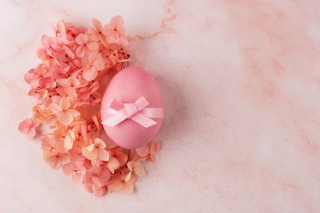Huevo de Pascua rosa con ramitas de hortensia sobre un fondo de mármol rosa
