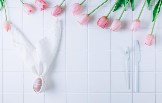 Huevo de pascua rosa teñido moderno en servilleta con flores de orejas de conejo en plato y cubiertos