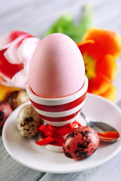 Foto huevo de pascua en soporte y flores de tulipán sobre fondo de madera