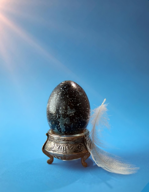 Huevo de pascua en un soporte teñido con tintes naturales con un fondo azul pluma