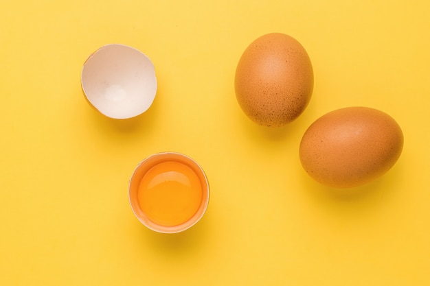 Un huevo roto y dos huevos enteros sobre una superficie amarilla. Un producto natural.