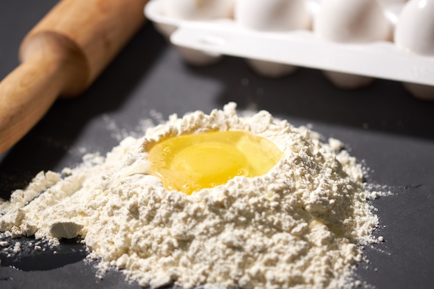 Foto huevo roto en harina, junto a un rodillo y huevos enteros.