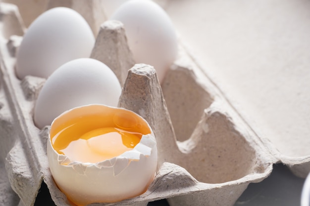 Huevo roto, yema de huevo, primer plano. Huevos en caja de cartón, embalaje ecológico. Cocinar en la cocina, en casa. Fondo.