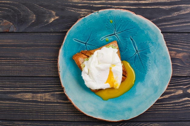 Huevo tostado y escalfado con aguacate en un plato en mesa de madera