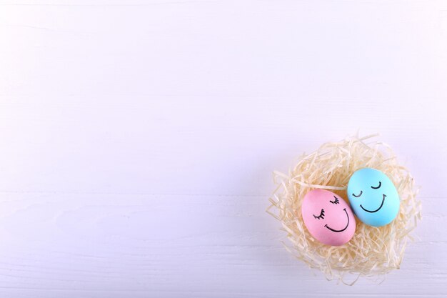 Huevos azules y rosados con sonrisas pintadas en el nido, tarjeta de felicitación de Pascua feliz.