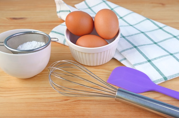 Huevos, batidor y utensilios de cocina sobre superficie de madera