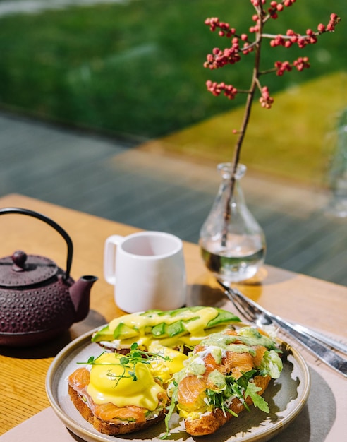 Huevos benedictinos sobre muffin inglés con mezcla de ensalada de lechuga y salmón ahumado y salsa holandesa