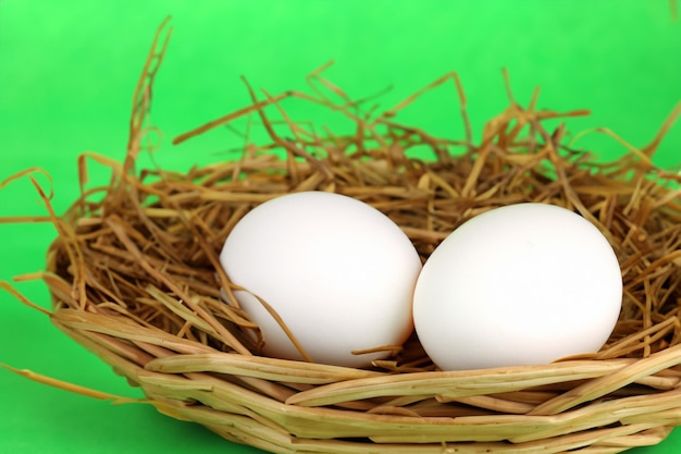 huevos blancos en un bascet de mimbre sobre paja sobre fondo verde de cerca