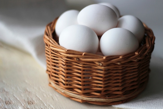 Huevos blancos en una cesta de mimbre en mesa de madera.