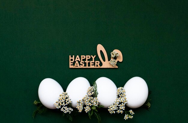 Huevos blancos festivos de Pascua con pequeñas flores blancas sobre un fondo verde Cerca hay una inscripción de madera Felices Pascuas