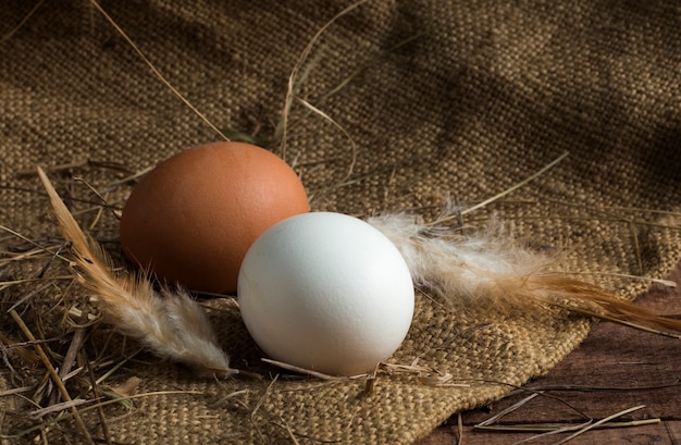 Huevos blancos y marrones con plumas sobre un fondo de madera marrón con arpillera.