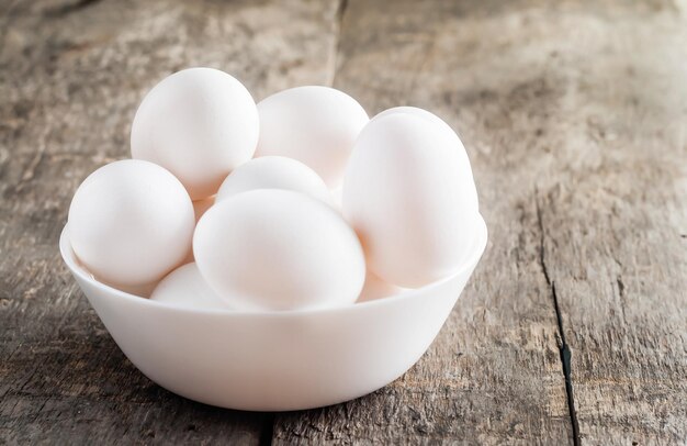 Huevos blancos de pollo crudo en un tazón blanco sobre fondo de madera