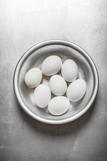 Huevos blancos en un recipiente sobre la mesa de metal.