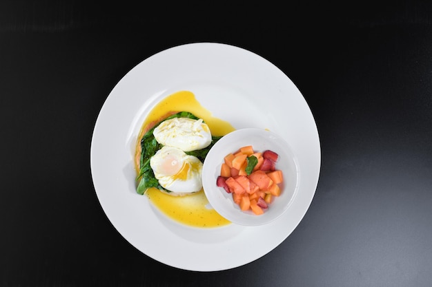 Foto huevos blandos sobre espinacas acompañados de una variedad de frutas