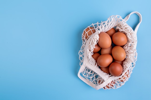 Huevos en una bolsa de compras blanca aislada sobre fondo azul vista superior plana pone con espacio de copia