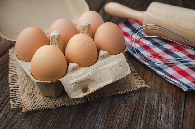 Huevos en cartón con batidor y rodillo en mesa de madera para cocinar y panadería concepto