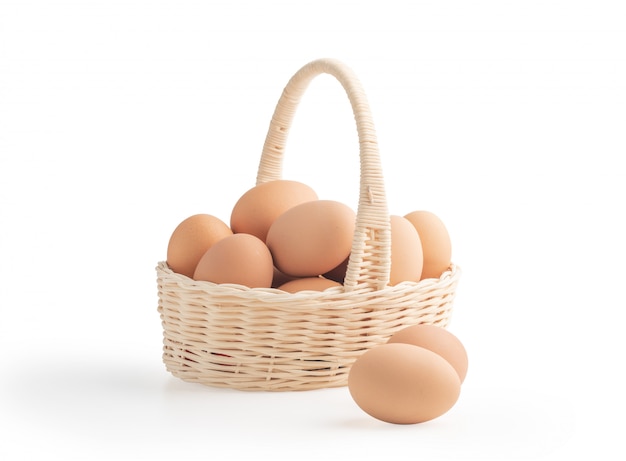 Huevos en la cesta de mimbre aislada en los fondos blancos