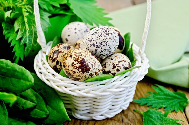 Huevos de codorniz en una canasta de mimbre blanco con ortigas y acedera, servilleta contra una tabla de madera