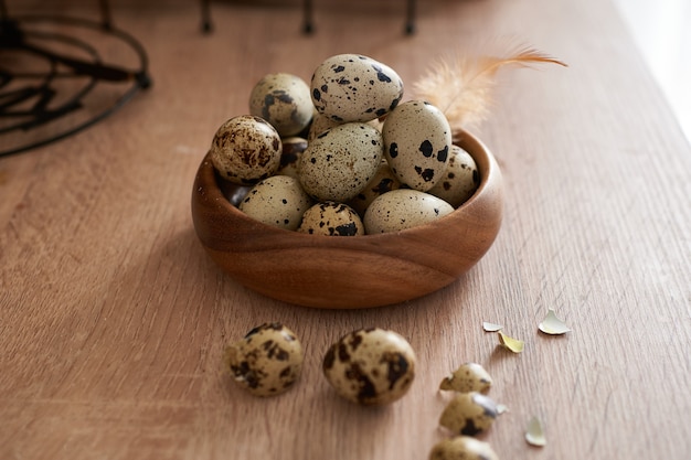 Huevos de codorniz en un cuenco de madera pintado con una pluma sobre una mesa de madera. Concepto de Pascua Espacio de copia