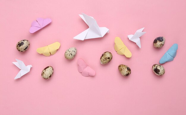 Huevos de codorniz y mariposas de origami palomas sobre fondo rosa pastel Composición de Pascua Vista superior