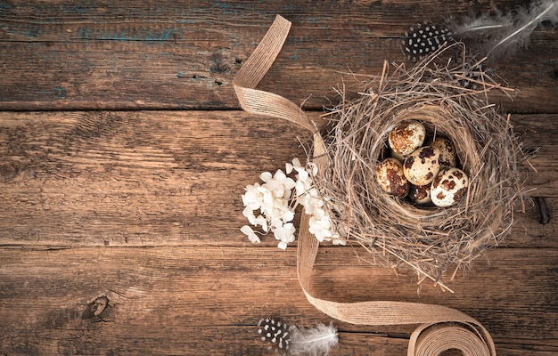 Huevos de codorniz en un nido de pájaro natural con flores y una cinta sobre un fondo de madera.