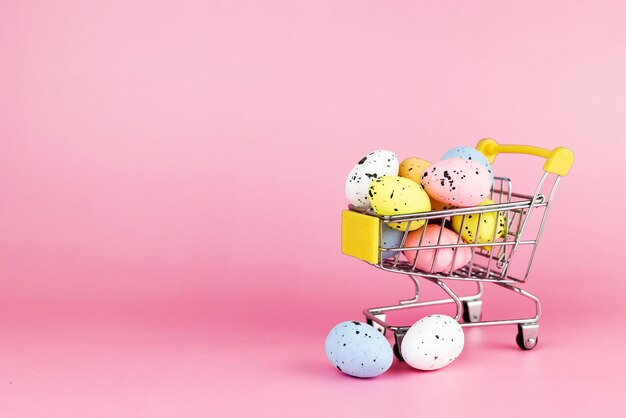 Huevos de codorniz de Pascua coloridos en carrito de compras sobre fondo rosa Espacio de copia Concepto mínimo de Pascua