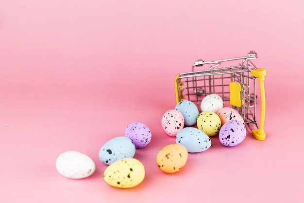 Huevos de codorniz de Pascua coloridos en carrito de compras sobre fondo rosa Espacio de copia Concepto mínimo de Pascua