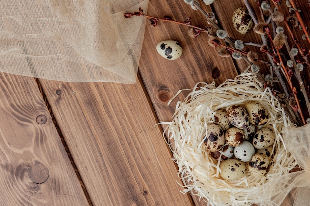 Huevos de codorniz de Pascua en nido y rama de sauce sobre un fondo de madera, espacio de copia