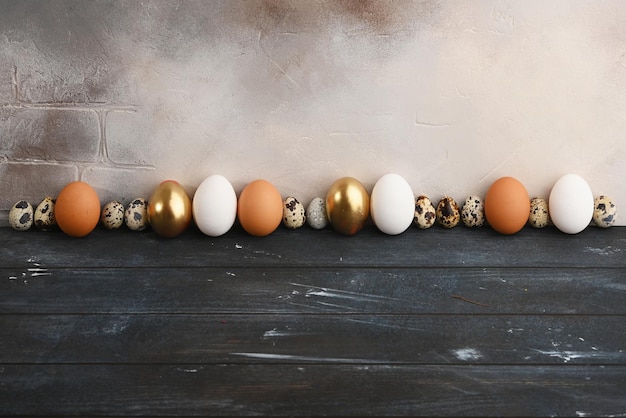 Huevos de codorniz y pollo de diferentes tamaños y colores se colocan en fila contra una pared gris envejecida Horizontal