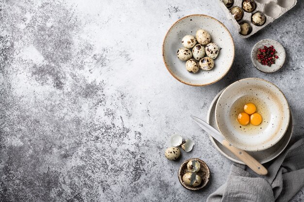 Huevos de codorniz rotos en un cuenco de cerámica sobre una mesa gris. Vista superior, lugar para texto.