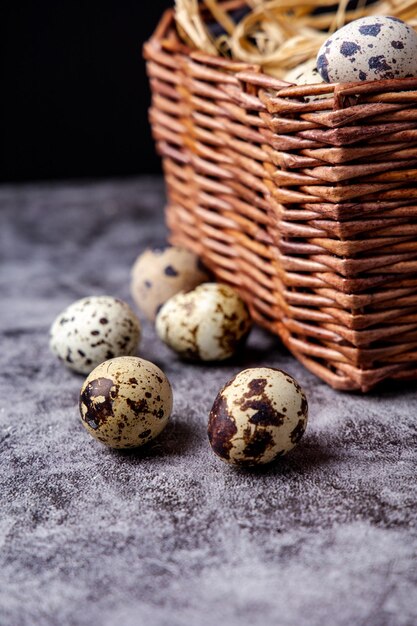 Huevos de codorniz sobre una superficie de piedra gris oscuro con la cesta al fondo