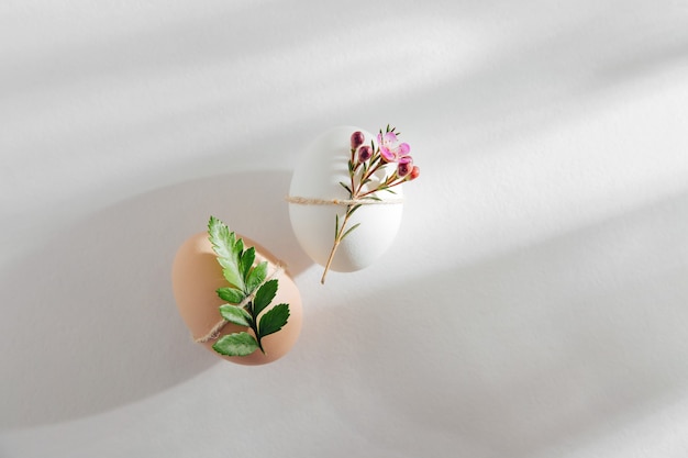 Huevos de colores naturales decorados con flores a la luz del sol de la mañana. Composiciones minimalistas con estilo en colores pastel. Concepto de Pascua.