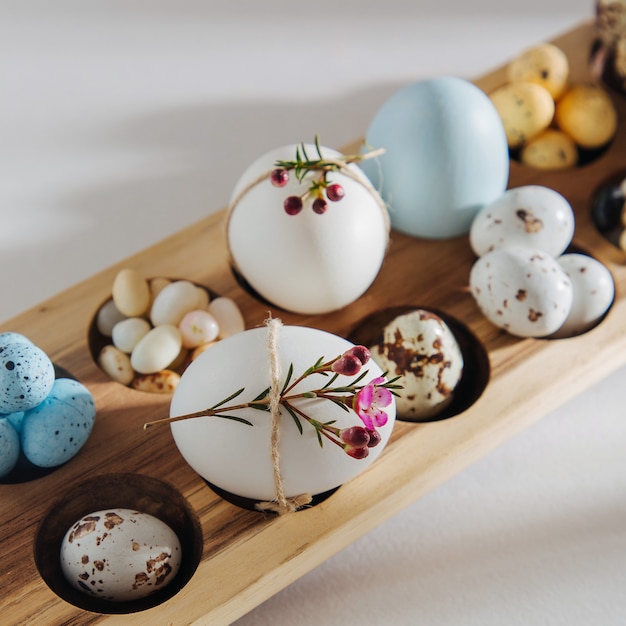 Huevos de colores naturales con flores, huevos de chocolate de pascua, caramelos y gominolas en caja de madera para huevos con luces solares. Composiciones con estilo.