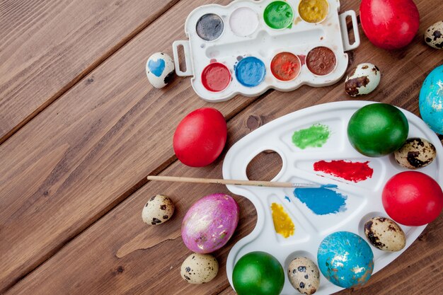 Huevos de colores y pintura sobre una mesa de madera, fondo de Pascua