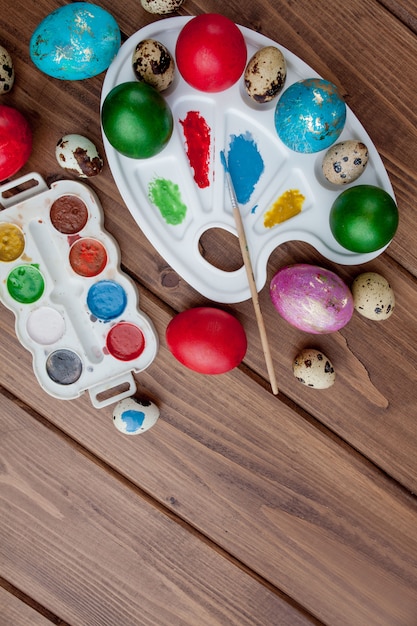 Huevos de colores y pintura sobre una mesa de madera, fondo de Pascua