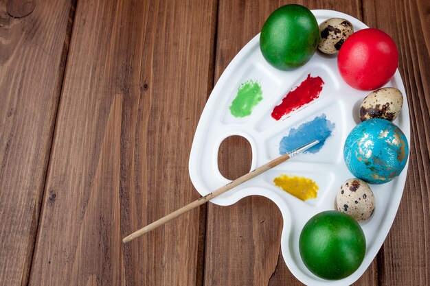 Huevos de colores y pintura sobre una mesa de madera, fondo de Pascua