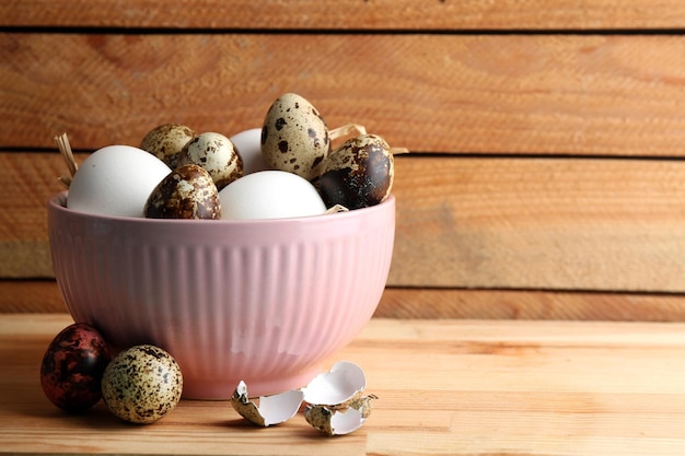 Huevos coloridos de aves en un recipiente sobre fondo de madera