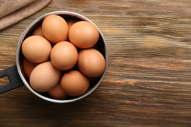 Huevos crudos en cacerola sobre mesa de madera