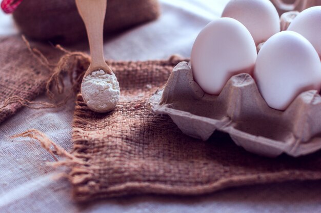 Huevos y una cuchara con harina sobre una tela de saco