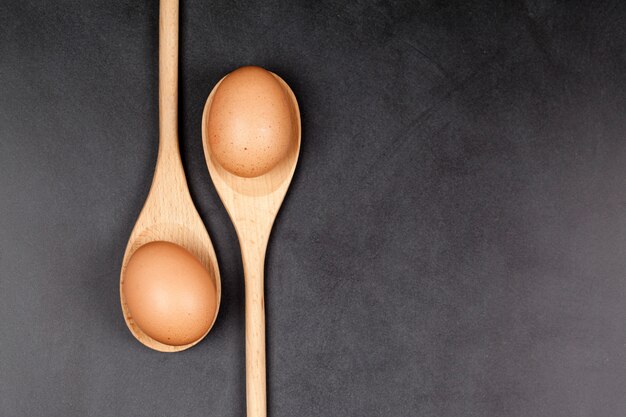 Huevos en cucharas de madera. Utensilio de la cocina para la torta, los pasteles o las galletas en fondo del tablero trasero.