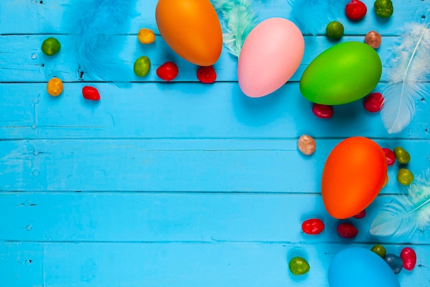 Huevos, dulces y plumas sobre un fondo de madera azul, lugar para el texto. Bodegón de Pascua.