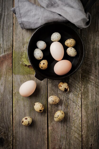 Huevos enteros de codorniz y gallina en una sartén pequeña de hierro fundido