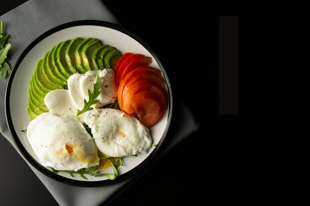 Huevos Escalfados De Aguacate. Comida y tomate sanos de desayuno en fondo negro.