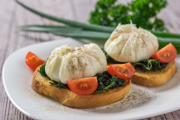 Huevos escalfados con pan y cebollas verdes en un plato blanco. Merienda vegetariana con huevos escalfados.